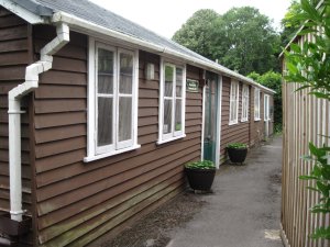 The Hall is a single story, wooden, brown and with windows facing out along the path. structure