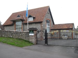 A brick building with very large windows, set behind a wall and with anniversary gates celebrating the Diamond Jubilee