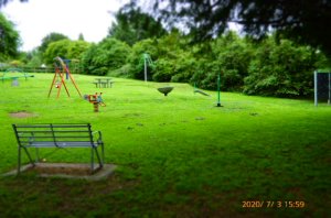 The area slopes gently up, is bordered by well established trees and has play equipment at the bottom, another fenced area above for a small BMZ course.