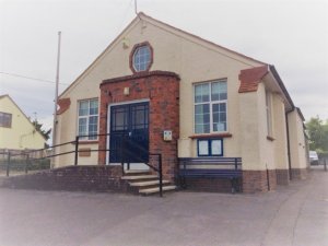 Coxley Memorial Hall is a single storey, 1920s built hall with access ramp, flagpole and painted white with brown decorative brickwork.