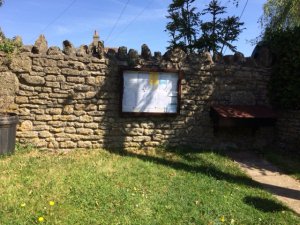 A wall-mounted notice board with patch of grass in front.