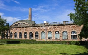 A long mill building with arched windows and chimney behind