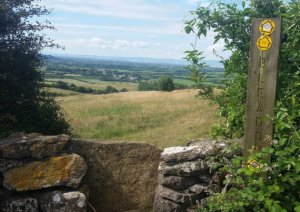 a stone stile and wooden sign directing walkers. Fields beyond